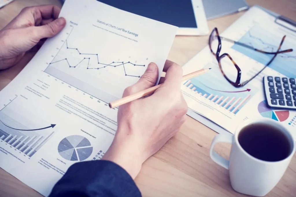 Hands analyzing financial charts with coffee