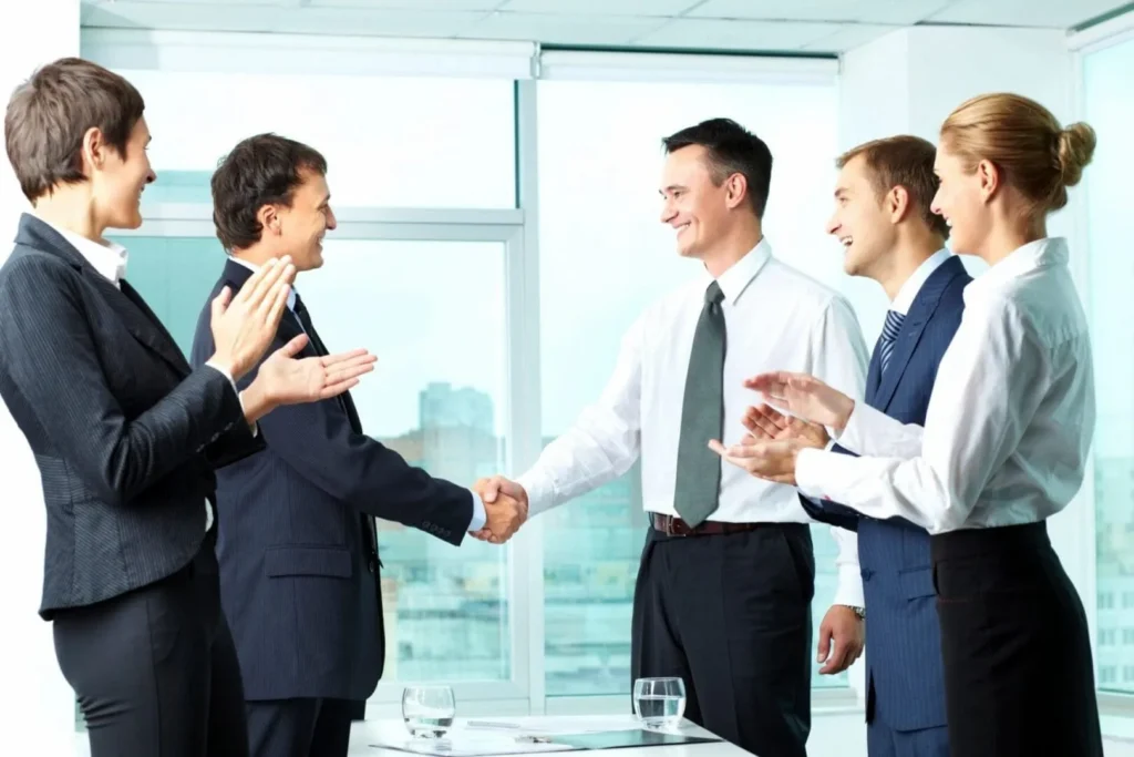 Businesspeople shaking hands while colleagues applaud