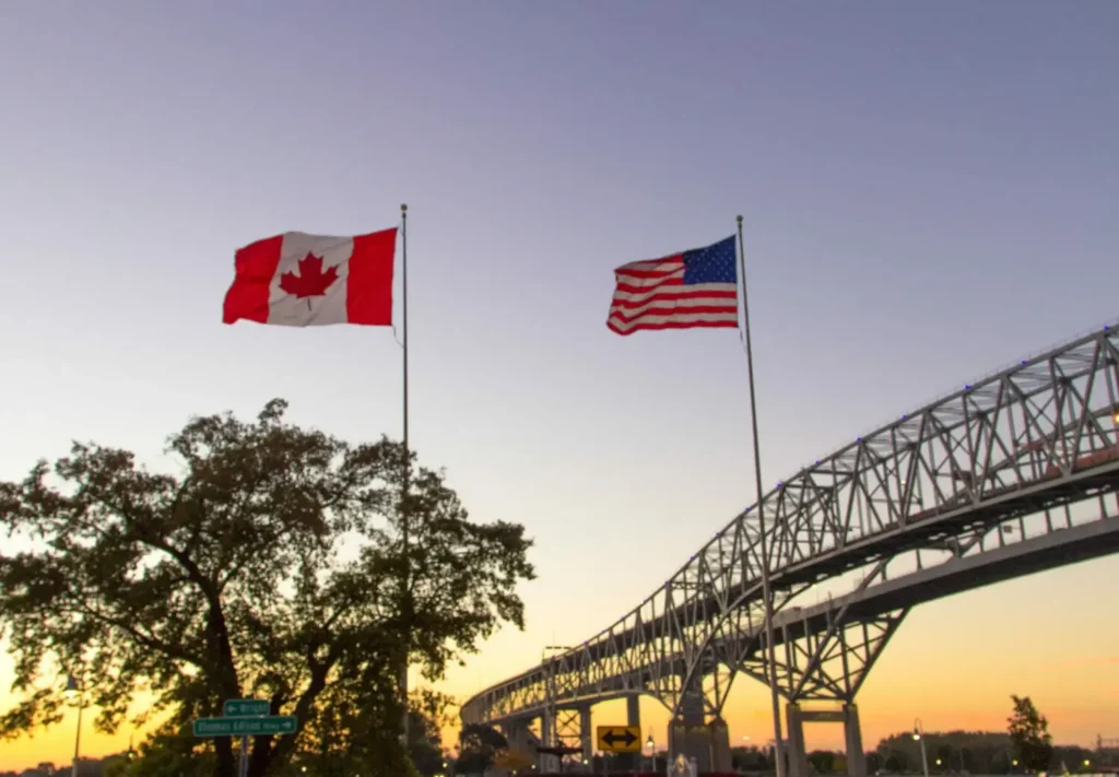 Canadian and American flags by bridge at sunset
